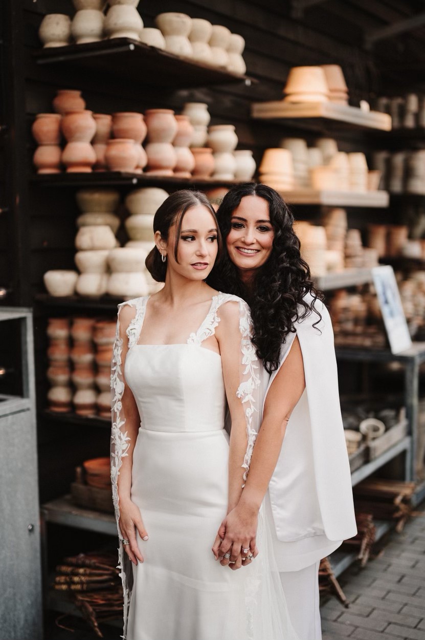 Two brides in white gowns holding hands, soft glam wedding day makeup