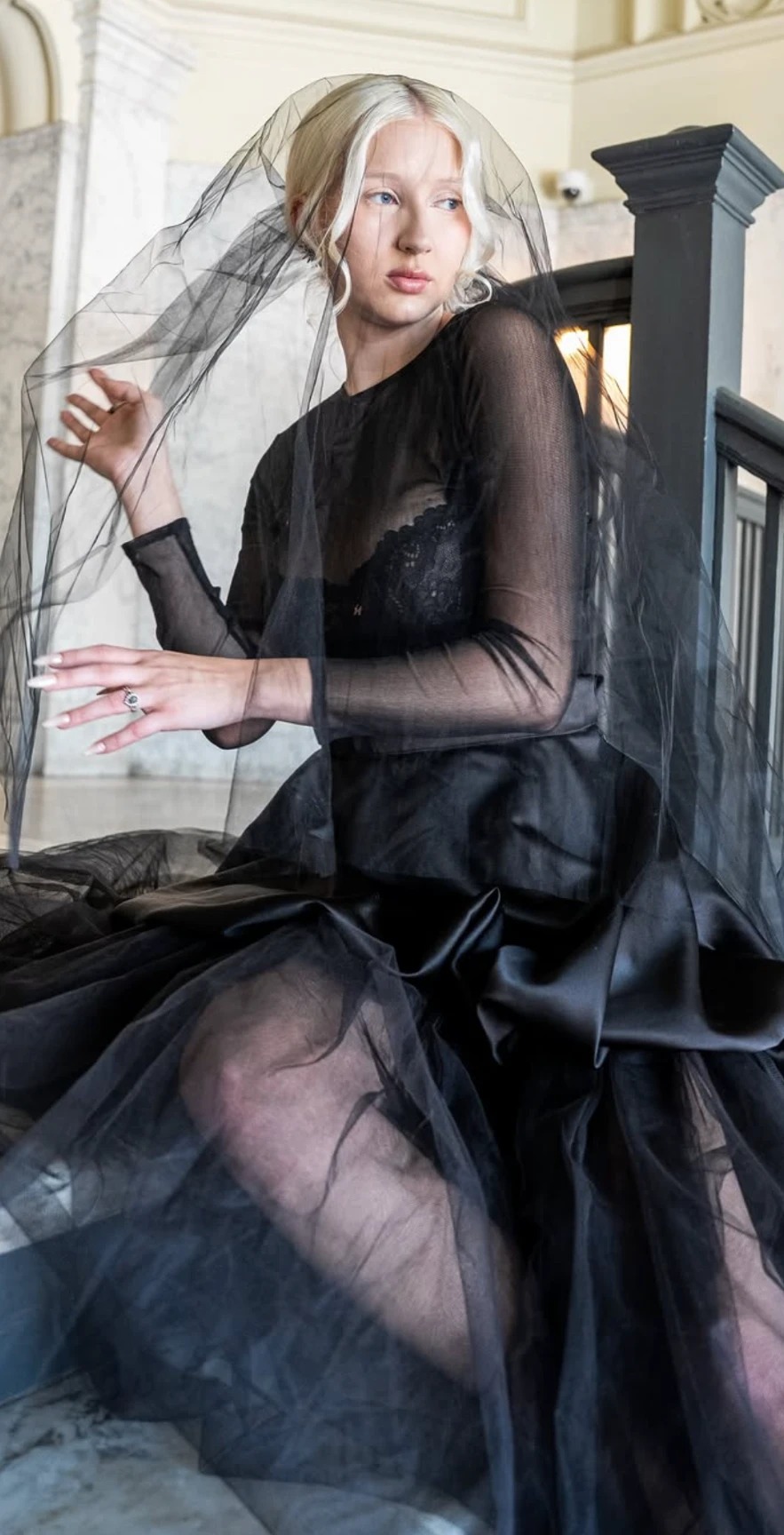 Editorial portrait of a model in a black tulle veil with luminous porcelain skin makeup